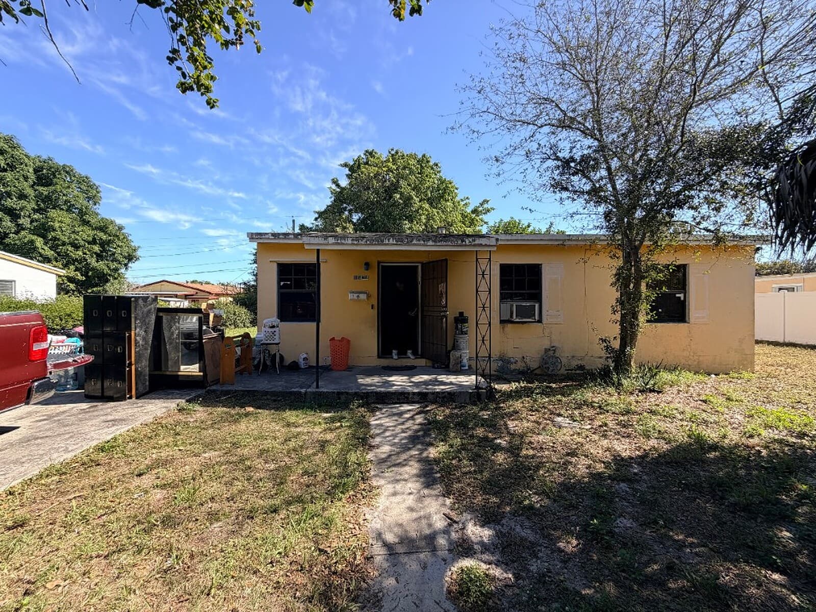 Distressed yellow Miami Gardens home with cluttered yard before cash sale