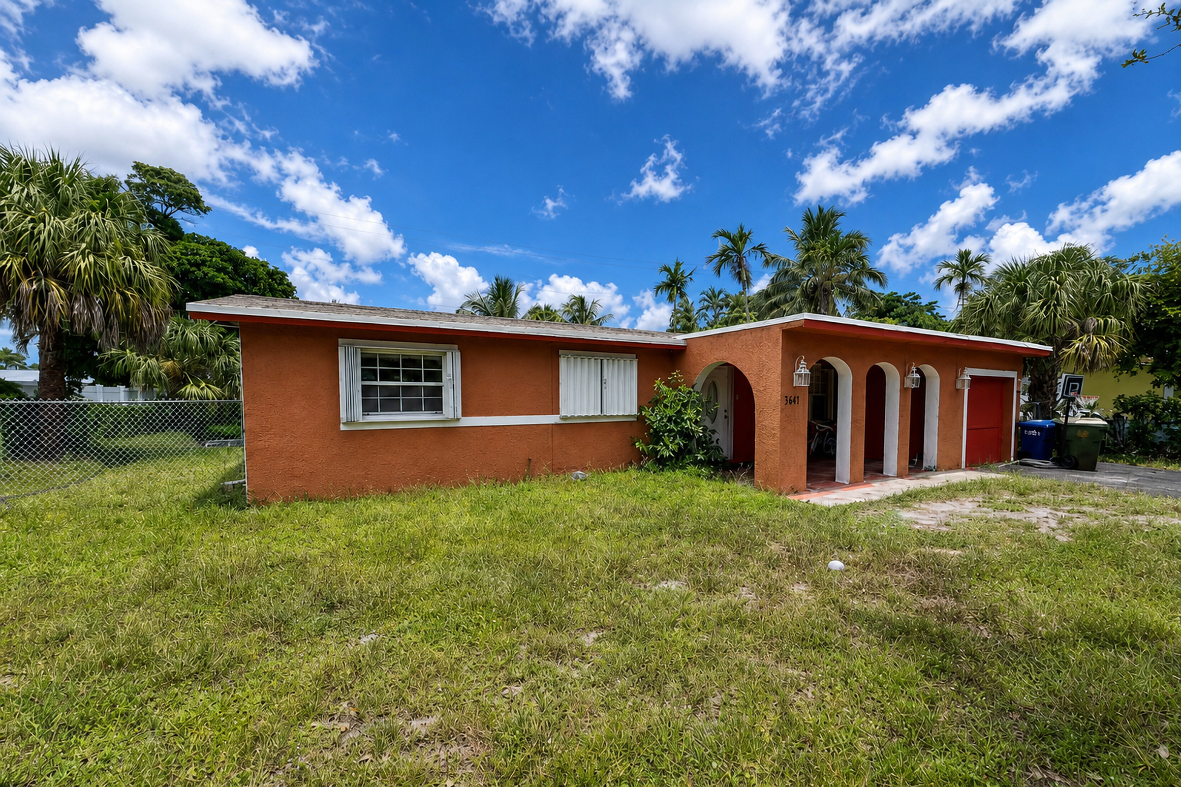 Orange stucco South Florida ranch home with arched porch, palms, and overgrown lawn