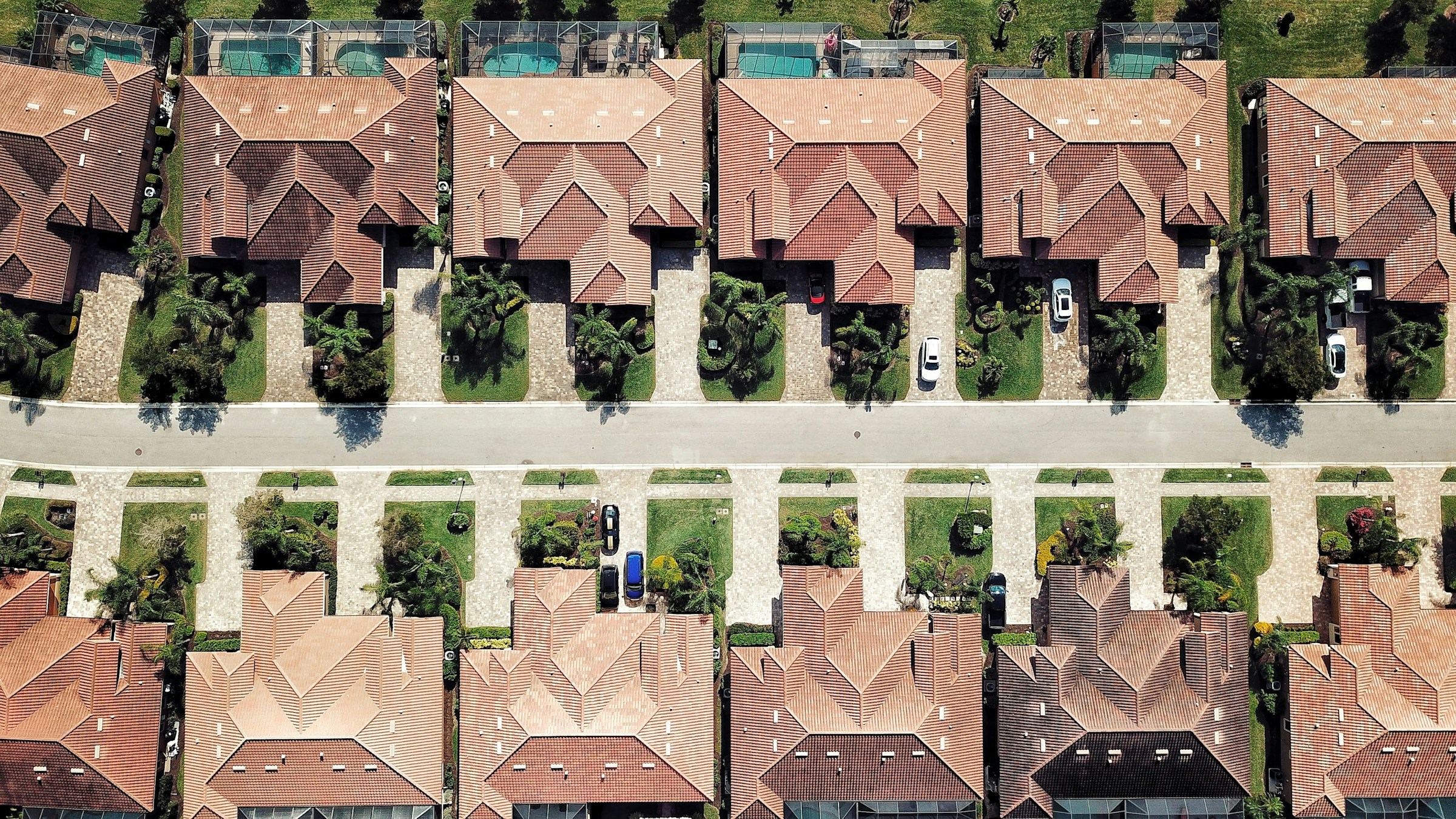 Aerial view of a Florida neighborhood with tile roofs, pool cages, and palm landscaping