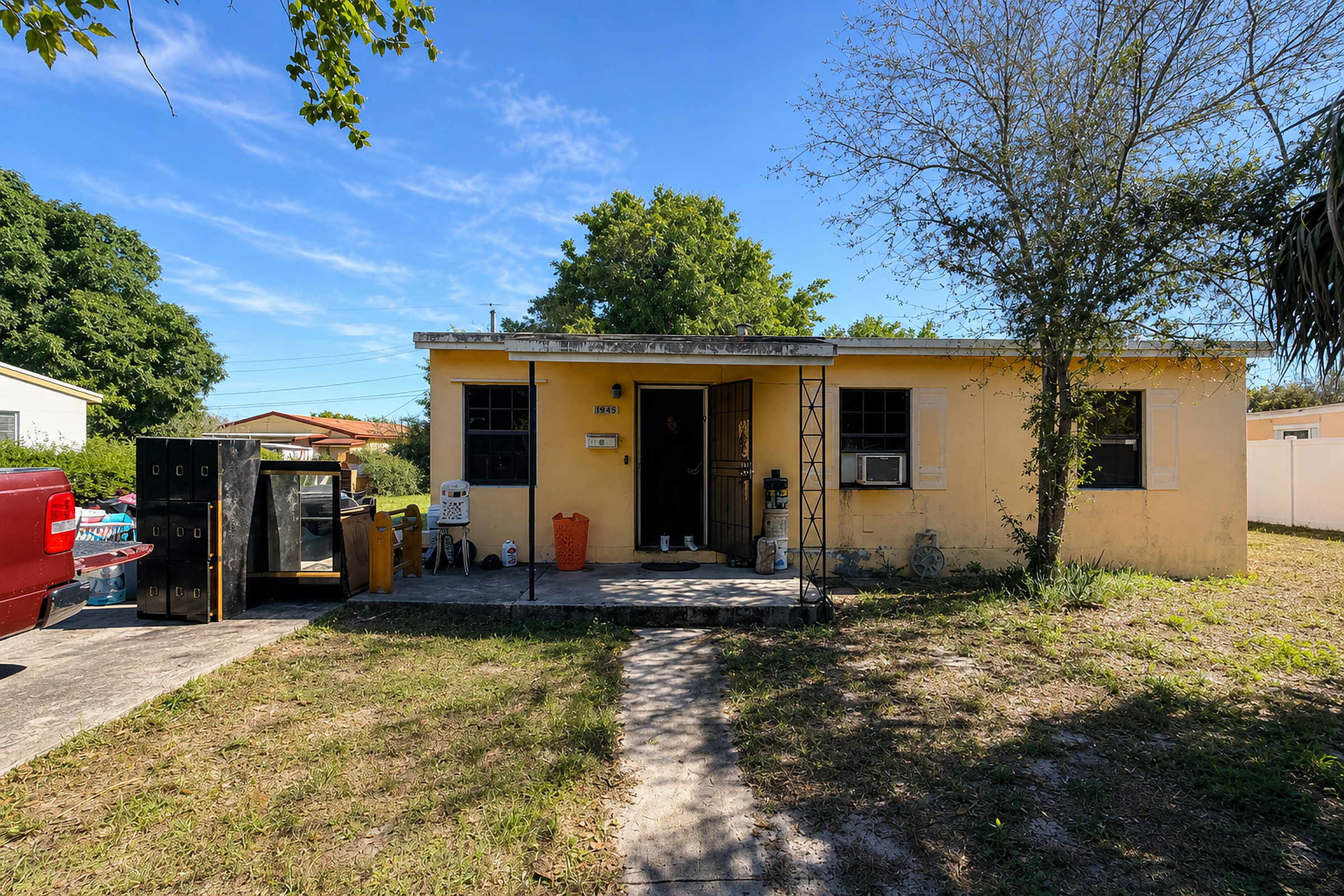 Distressed yellow South Florida ranch house with cluttered yard and open front door